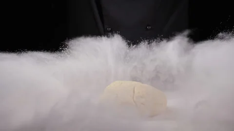 Cloud of white flour caused by chef in dark suit slamming glob of dough onto the Stock Footage 169401410