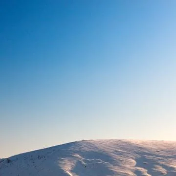 Cloudless blue sky above snow-covered hillside. View at sunset. Stock Photos