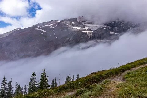 Clouds and mountain top with snow and meadow and trees below Stock Photos