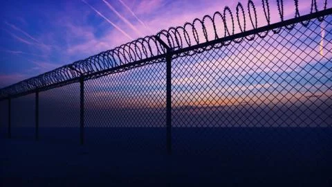 Clouds and a sunset can be seen through the metal prison fence with barbed wire Stock Illustration