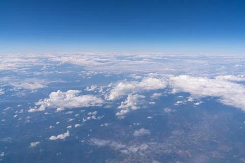Clouds are spread out across the landscape below. The sky is clear and blue.. Stock Photos
