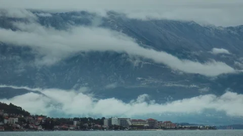 Clouds blanket the mountains and create a serene view over the lakeside town at Stock Footage 313731556