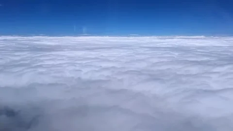 Clouds blanket the sky with a bright blue horizon, seen from above during a sere Stock Footage 285134381