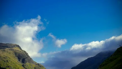 Clouds blowing over mountain tops with a blue sky in slow motion Stock Footage