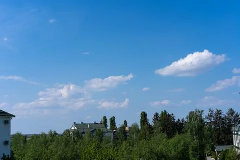 Clouds in the blue sky above the trees and houses. Stock Photos
