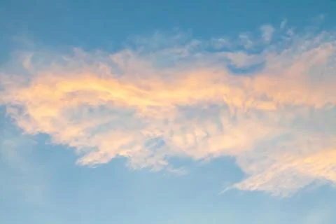Clouds on a blue sky backlit in yellow and orange at early sunset. concept .. Stock Photos