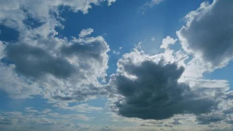 Clouds in blue sky slowly move and change shape. Sun rays shine throughclouds 写真素材