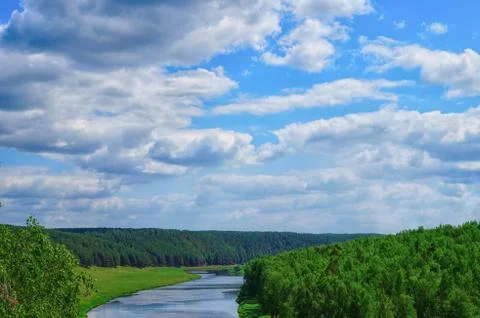 Clouds on clear sky with green trees along fast river Stock Photos