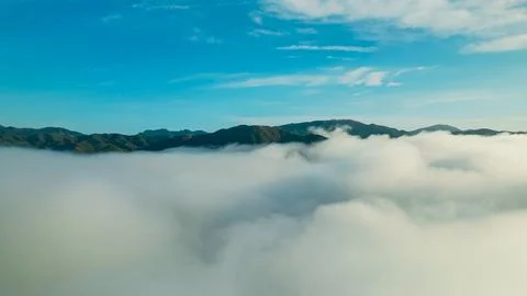 Clouds cover mountain range under bright blue sky at sunrise Stock Photos