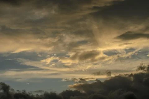 Clouds dance in the evening sky while warm hues of gold and grey blend duri.. Stock Photos