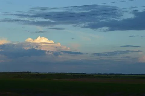 Clouds drift above the horizon during sunset over a vast open field in the Stock Photos
