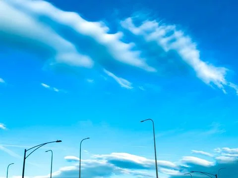 Clouds drift across a bright blue sky over a road with streetlights in a su.. Stock Photos