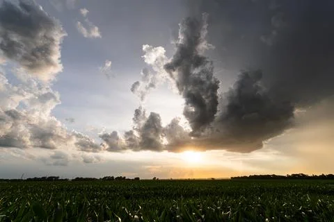 Clouds drift across the setting sun over farmland, creating a dramatic sky wi Stock Photos