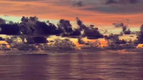 Clouds drift across a vibrant sunset over a calm ocean reflecting warm colors Stock Footage 338282752