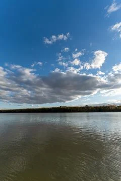 Clouds drift over a calm river under a clear blue sky in the afternoon ligh.. Foto stock