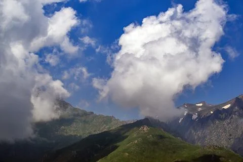 Clouds drift over mountain peaks with green ridges and snowy patches Fotos Stock