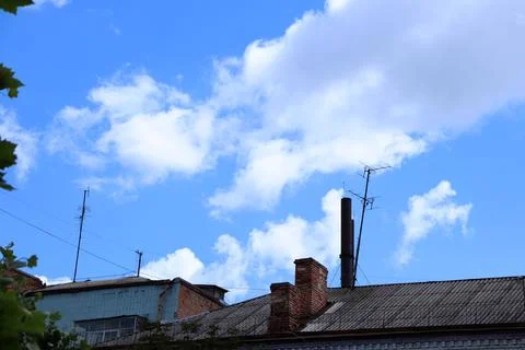 Clouds drift over rooftops in a city during daytime under a clear blue sky Foto stock