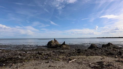 Clouds drifting across a blue sky above a calm coastal shore with weathered Stock Footage 346048606