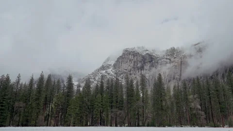 Clouds drifting over granite cliff above snowy meadow timelapse Video stock 347988443