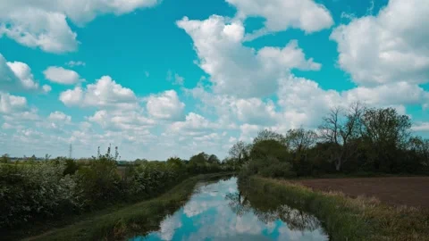Clouds drifting in timelapse above tranquil countryside canal with mirrored 库存影片 334662500