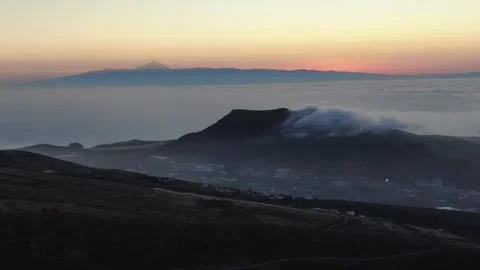 Clouds enveloping mountain peak at sunset with Teide volcano in background Stock Footage 313443873