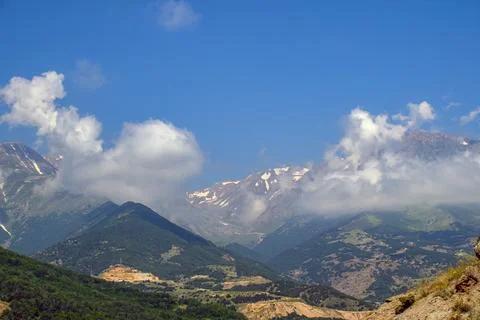 Clouds float above mountain ridges with patches of snow Stock Photos