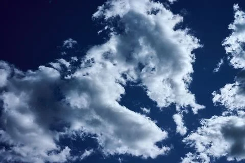 Clouds float in the blue sky with various shapes, casting shadows over the pa Stock Photos