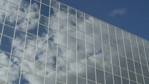 Clouds floating across the blue sky are reflected in the windows of a tall glass Stock Footage 125450091