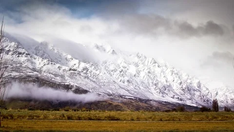 Clouds floating over snow covered mountains and green landscape Stock Footage 76104743