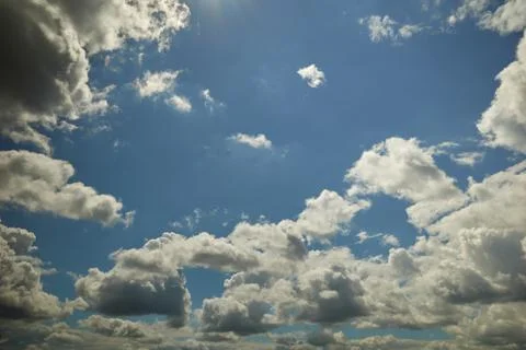 Clouds floating overhead in the blue sky lightened by sunrays Stock Photos