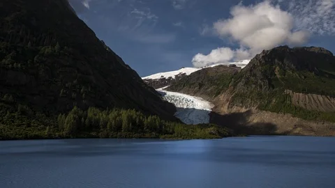 Clouds flowing over glacier in lush green mountains with a lake 8K time lapse Stock Footage 114000786