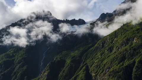 Clouds flowing over lush green mountains with waterfall 8K time lapse Stock Footage 113998768