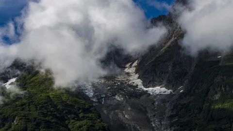 Clouds flowing over lush green mountains with waterfall 8K time lapse Stock Footage 114000032