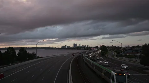 Clouds fly above freeway traffic &amp; trains at dusk. City in background. Stock Footage 252057307