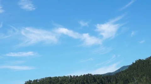 Clouds flying in a deep blue sky with mountains in background Stock Footage 76950754
