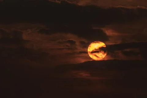 Clouds in front of sun during sunset in orange sky Stock Photos