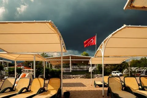 Clouds gather over beach area with sun loungers and Turkish flag flying in wi 스톡 사진