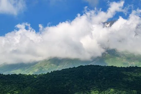 Clouds hover over forested mountain range under clear blue sky Fotos Stock
