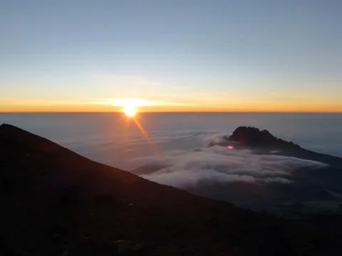 Clouds hover over the mountains. The sun is setting on the distant horizon Stock Photos