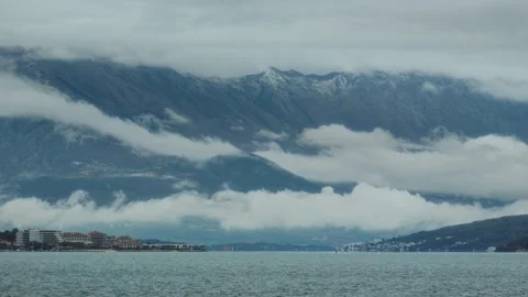 Clouds hug mountains above serene water near coastal town in Montenegro Stock Footage 313731552