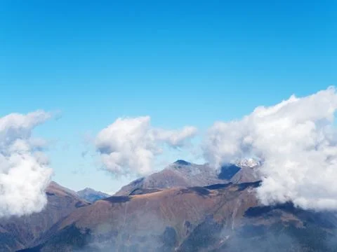 Clouds lowered on mountain peaks on a clear sunny day Stock Photos