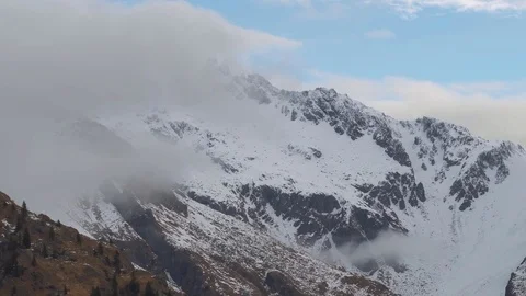 The clouds move over the snow-covered mountain, gradually going down 스톡 동영상 77913448