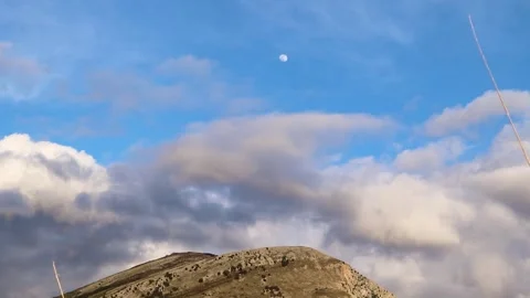 Clouds Move Slowly Across the Sky With a Bright Moon High Above a Mountain Stock Footage 323803940