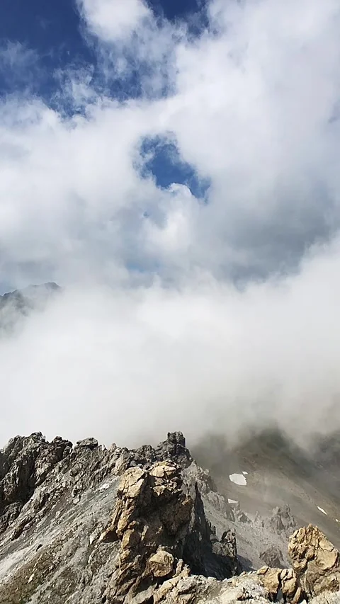 Clouds moving around rocky alpine peaks and ridges in a slow-motion manner Video stock 248379416