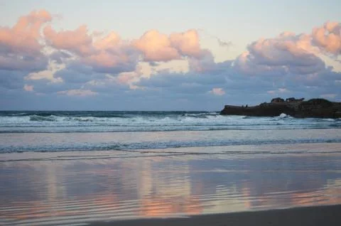 Clouds over a beach at sunset, with two men fishing. Stock Photos