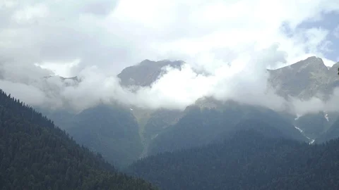 Clouds over mountain peaks with evergreen trees and blue sky Stock Footage 114897717