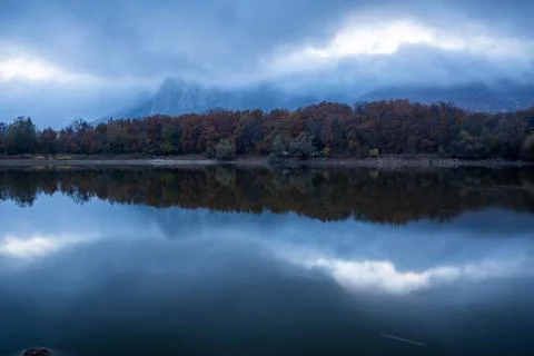 Clouds over the mountains and forest are reflected in the lake after sunset Stock Photos