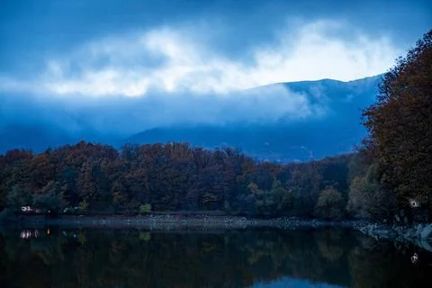 Clouds over the mountains and forest are reflected in the lake after sunset Stock Photos
