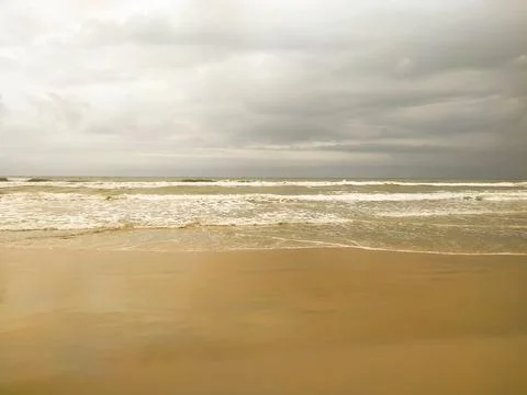 Clouds over waves on the sand beach Stock Photos