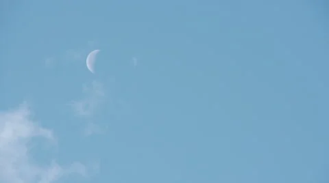 Clouds passing in front of a white moon against a blue sky Stock Footage 53236924